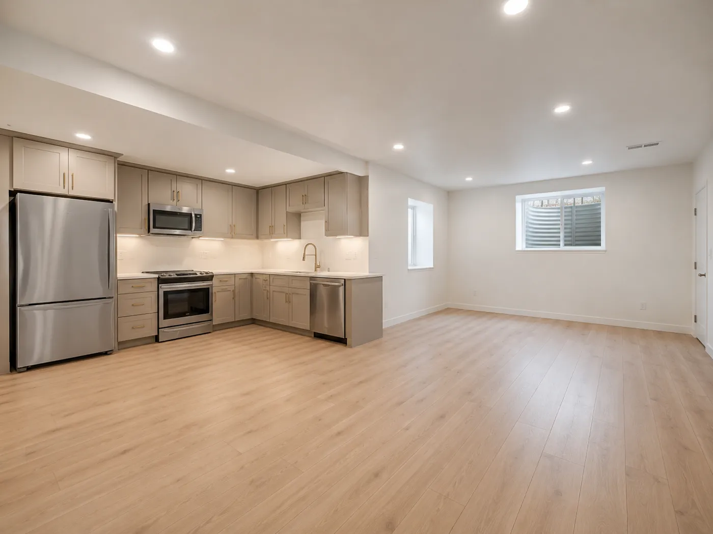 Open basement family room and kitchen with taupe shaker cabinets, stainless appliances, and light wood-look flooring
