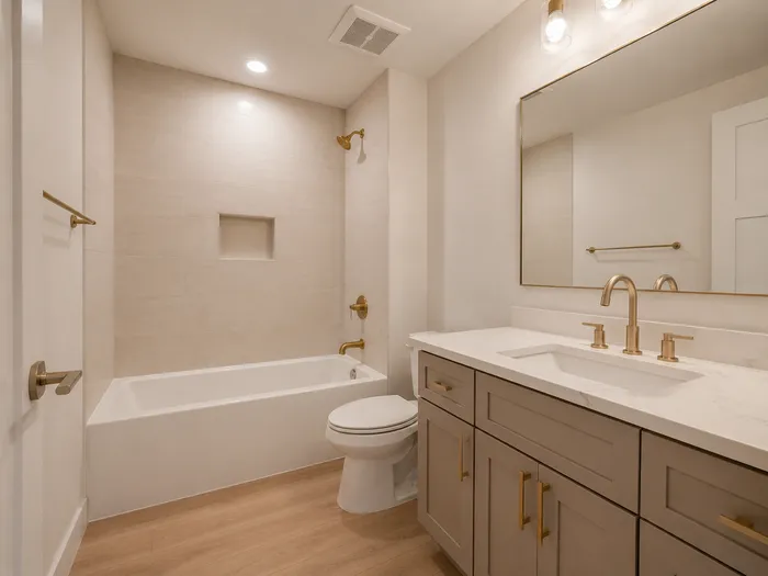 Basement bathroom with tiled tub shower, taupe vanity, and brass fixtures