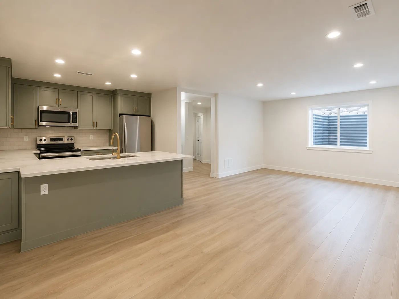 Sage green basement kitchenette with island, brass faucet, and stainless appliances
