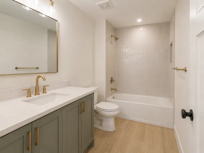 Basement bathroom with sage vanity, brass fixtures, and glossy tiled tub shower